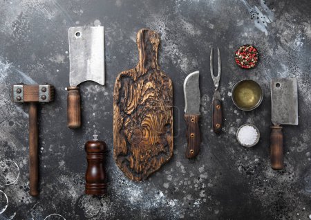 Photo for Kitchen meat utensils set on dark kitchen background. Meat cleaver,fork,knife with wooden tenderizer and various herbs and oil. - Royalty Free Image