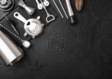 Foto de Coctelera de acero, colador, jigger y exprimidor de madera con desorden y abridor de vino en piedra negra. - Imagen libre de derechos