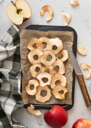 Foto de Anillos de manzana secos dulces en bandeja para hornear con cuchillo y toalla de cocina. - Imagen libre de derechos