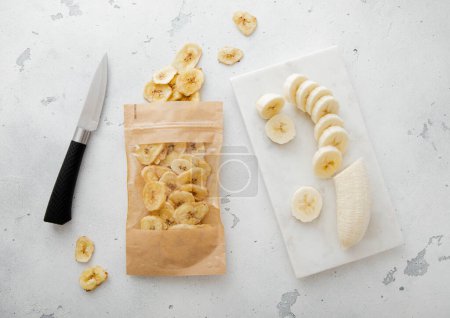 Foto de Pack de chips secos de plátano sano con cuchillo y plátano crudo.. - Imagen libre de derechos