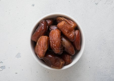 Dried sweet organic dates in ceramic bowl on light background.