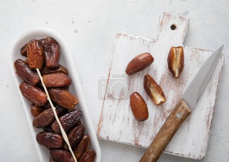 Organic dried sweet dates with chopping board and knife on white kitchen background.