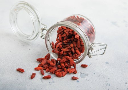 Foto de Tarro de vidrio con bayas rojas secas de goji dulce sobre fondo de cocina blanco. - Imagen libre de derechos