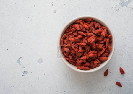 Téléchargez les photos : Baies de goji sucrées rouges séchées dans un bol en céramique sur fond de cuisine blanche. - en image libre de droit