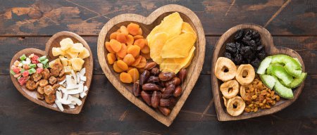 Téléchargez les photos : Fruits secs doux et sains dans des assiettes en bois en forme de coeur sur fond en bois. - en image libre de droit