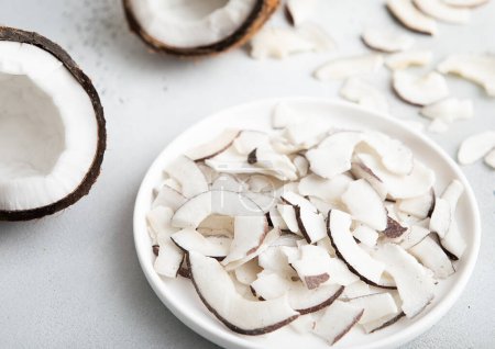 Teller mit getrockneten Bio-Kokosscheiben Chips und ganzen reifen Kokosnüssen auf hellem Hintergrund.