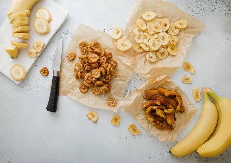 Foto de Varios crujientes y masticables rodajas de plátano y patatas fritas snack con plátano crudo y cuchillo. - Imagen libre de derechos