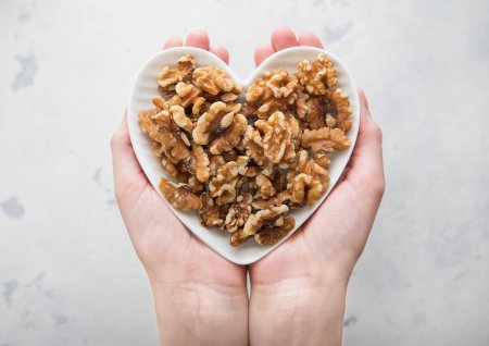 Photo for Female hands holding heart shaped plate with healthy peeled walnut nuts on light background. - Royalty Free Image