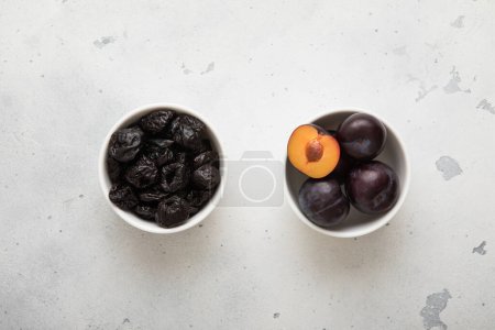 Téléchargez les photos : Deux bols avec pruneaux séchés et prunes crues mûres sur fond clair.. - en image libre de droit