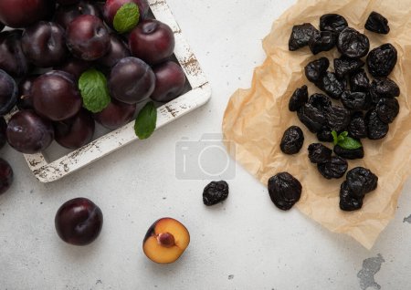 Téléchargez les photos : Pruneaux doux séchés avec prunes mûres dans une boîte en bois sur fond de cuisine légère. - en image libre de droit
