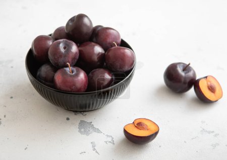 Photo for Bowl with raw ripe purple plums on light kitchen background.Macro. - Royalty Free Image