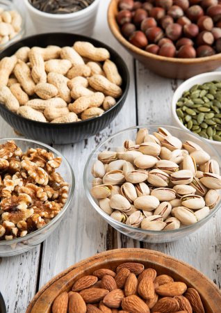 Photo for Mixed raw nuts and seeds in bowls on kitchen table.Peanut,hazelnut,walnut,almonds,pistachio,sunflower,pumpkin,chia and cashew. - Royalty Free Image