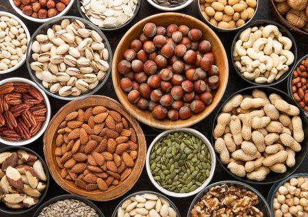 Photo for Mixed healthy nuts and seeds in various bowls on dark kitchen table.Peanut,hazelnut,walnut,almonds,pistachio,sunflower,pumpkin,chia and cashew. - Royalty Free Image