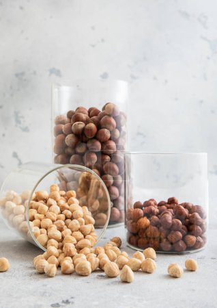 Photo for Glass jars with healthy raw hazelnut whole and peeled nuts on white kitchen table. - Royalty Free Image