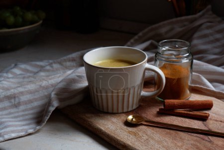 Photo for Golden latte, cup of hot turmeric latte with cinnamon sticks on wooden cutting board - Royalty Free Image