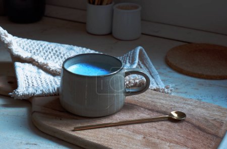 Photo for Blue spirulina latte in ceramic cup with a spoon on a wooden cutting board background - Royalty Free Image