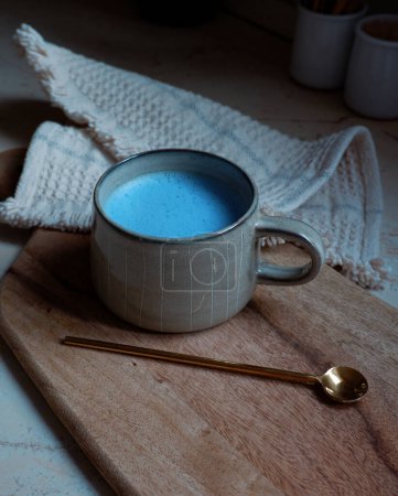 blaue Spirulina Latte in Keramiktasse mit einem Löffel auf einem hölzernen Schneidebrett Hintergrund