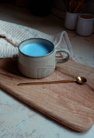 Photo for Blue spirulina latte in ceramic cup with a spoon on a wooden cutting board background - Royalty Free Image