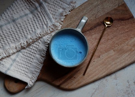 Téléchargez les photos : Latte spiruline bleue dans une tasse en céramique avec une cuillère sur un fond de planche à découper en bois - en image libre de droit
