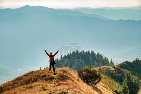 Foto de Happy woman with raised arms on the hiking trail in the mountains. Travel, active lifestyle and exploring - Imagen libre de derechos