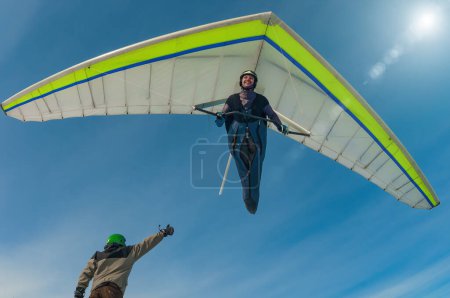 Aerial stunt. Hang glider pilot gives high five to his friend standing on the ground with thumb up. Beauty of extreme sports
