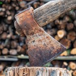 Old rusty axe with firewood stacks on the background.