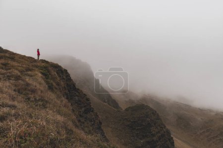 Téléchargez les photos : Femme solitaire debout sur le bord. Femme sur la montagne regarde vers le bas sur la vallée brumeuse - en image libre de droit