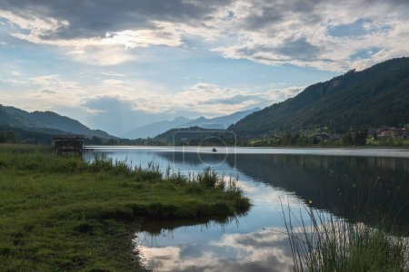 Téléchargez les photos : Lac alpin calme avec reflet du ciel au coucher du soleil. Les pêcheurs rêvent. Lac Weissensee, Autriche. - en image libre de droit