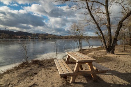 Téléchargez les photos : Banc et table du parc Woden sur la côte de la rivière gelée par temps ensoleillé au début du printemps - en image libre de droit