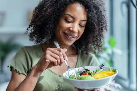 Photo for Shot of beautiful woman eating healthy salad while sitting on couch at home. - Royalty Free Image