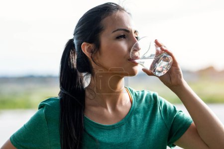 Foto de Tiro de mujer joven deportiva beber vaso de agua en el parque. - Imagen libre de derechos