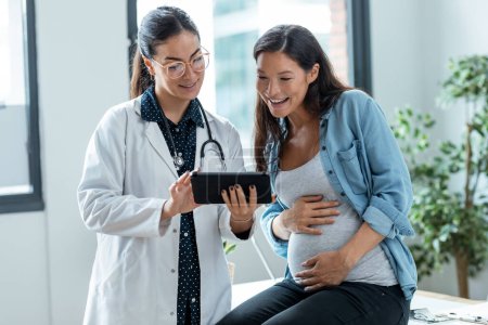 Foto de Inyección de médico ginecólogo femenino que muestra a la mujer embarazada ultrasonido escanear bebé con tableta digital en consulta médica. - Imagen libre de derechos
