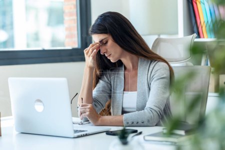 Photo for Shot of exhausted young business woman with headache while working with laptop in the office. - Royalty Free Image