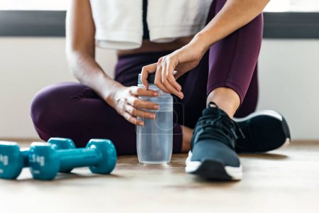 Photo for Close up of sporty woman holding water after exercises resting in the floor at home. - Royalty Free Image
