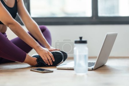 Foto de Tiro de mujer deportiva haciendo ejercicios de yoga siguiendo clases de gimnasia en línea en la sala de estar en casa. - Imagen libre de derechos