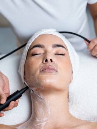 Foto de Shot de cosmetólogo hace que el procedimiento de una limpieza ultrasónica de la piel facial de una hermosa mujer joven en el centro de spa. - Imagen libre de derechos