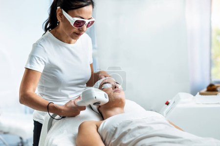 Photo for Shot of therapist cosmetologist makes laser treatment for woman's face in spa beauty clinic. - Royalty Free Image
