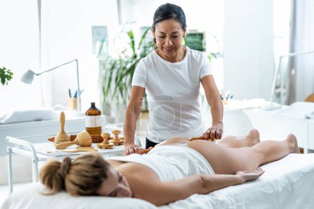 Téléchargez les photos : Shot of therapist woman doing back massage with wooden balls to a pretty woman on the spa center - en image libre de droit