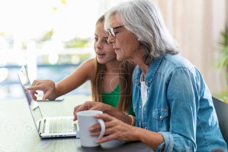 Téléchargez les photos : Shot of happy granmother shopping online with credit card using laptop with her granddaughter at home. - en image libre de droit