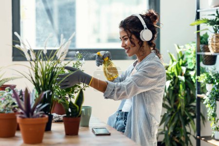 Téléchargez les photos : Shot of beautiful smiling woman arranging plants and flowers while listening music in a greenhouse - en image libre de droit