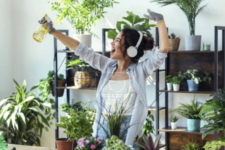Foto de Fotografía de una hermosa mujer sonriente arreglando plantas y flores mientras baila en un invernadero - Imagen libre de derechos