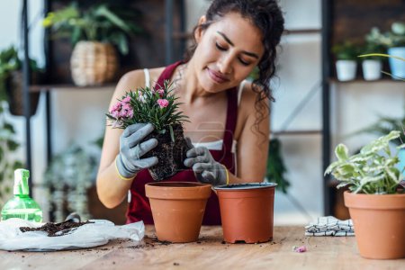 Foto de Shot of influencer woman arranging plants and flowers while recording a tutorial video with smartphone in a greenhouse - Imagen libre de derechos