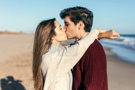 Photo for Shot of beautiful couple in love kissing each other while enjoying the day in a cold winter on the beach. - Royalty Free Image
