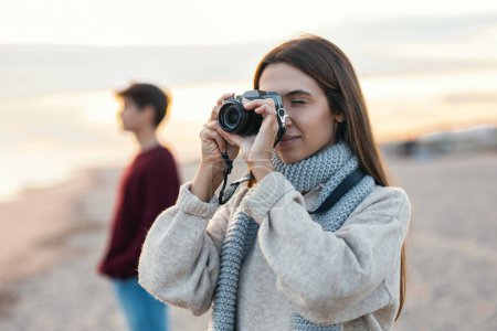 Téléchargez les photos : Prise de vue de jeunes couples heureux prenant des photos avec appareil photo sur un hiver froid à la plage. - en image libre de droit