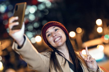 Foto de Fotografía de una joven turista riendo y tomando una foto selfie con teléfono móvil en la ciudad por la noche - Imagen libre de derechos