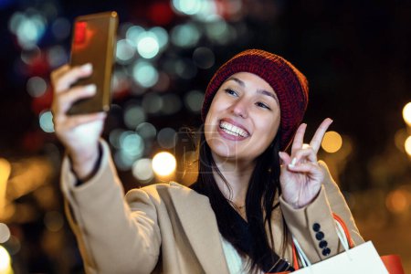 Foto de Fotografía de una joven turista riendo y tomando una foto selfie con teléfono móvil en la ciudad por la noche - Imagen libre de derechos