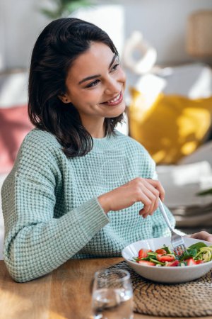 Foto de Retrato de una hermosa mujer sonriente comiendo ensalada saludable en casa. - Imagen libre de derechos