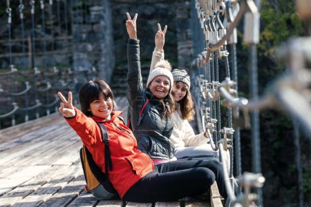 Téléchargez les photos : Prise de vue de belle famille faisant signe de victoire au photographe assis sur un pont dans la forêt de montagne - en image libre de droit