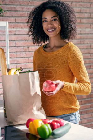 Foto de Tiro de mujer hermosa feliz sosteniendo bolsa de cartón con compras de salud en la cocina en casa - Imagen libre de derechos