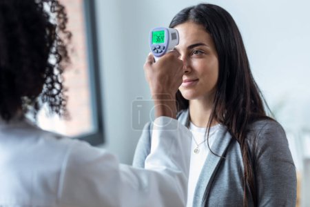 Photo for Shot of cheerful beautiful female doctor taking woman patient temperature with thermometer in medical consultation - Royalty Free Image